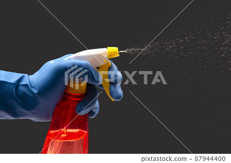 water sprayer bottle in a hand in a protective glove spraying liquid on a dark background water sprayer bottle in a hand in a protective glove spraying liquid on a dark background 87944400