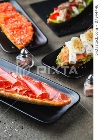 Traditional Spanish breakfast. Tostada with different toppings on a dark background Traditional Spanish breakfast. Tostada with different toppings on a dark background 87944446