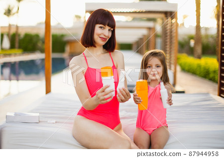A charming young mother sitting with her daughter in a gazebo near swimming pool A charming young mother sitting with her daughter in a gazebo near swimming pool 87944958