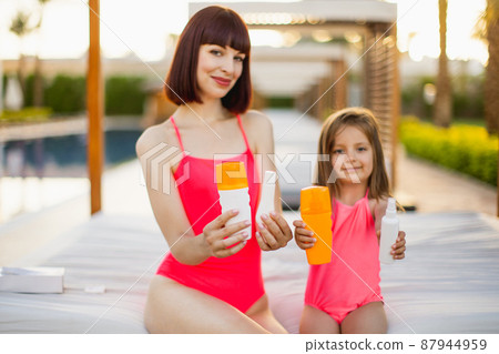 Focus on tube of sunscreen or moisturizer or sun block in the hands of a mother and her daughter 87944959