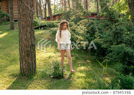Relaxed tween girl walking in green park of country house on summer day 87945398
