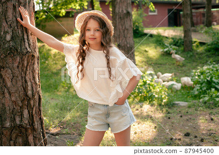 Preteen girl leaning of tall tree trunk in green courtyard of country house 87945400