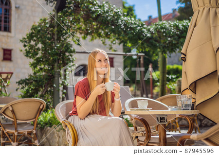 Young woman tourist drinks cofee in the old town of Budva. Travel to Montenegro concept Young woman tourist drinks cofee in the old town of Budva. Travel to Montenegro concept 87945596