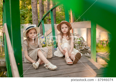 Two little girls resting on wooden bridge over pond in summer country estate 87946074