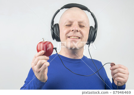 bald man with headphones listens to music through a red apple player. 87946469