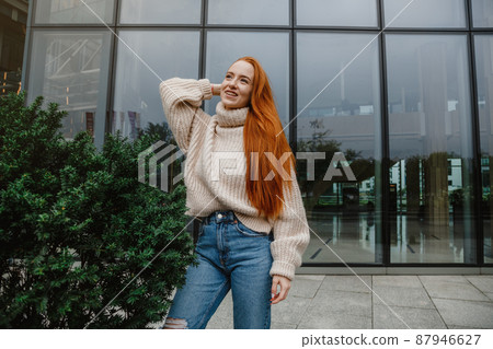 Portrait of successful happy woman on her way to work on street. Outdoor portrait of young beautiful natural redhead girl, very long hair, posing in street of city. Fashion girl with long red hair. Portrait of successful happy woman on her way to work on street. Outdoor portrait of young beautiful natural redhead girl, very long hair, posing in street of city. Fashion girl with long red hair. 87946627