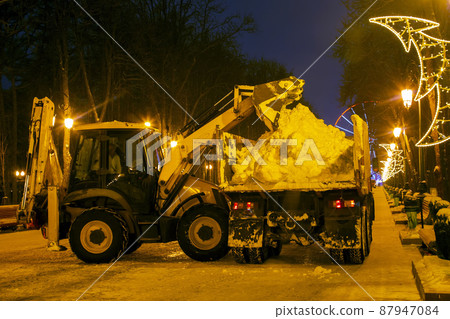 cleaning snow in the park in winter with a tractor in the evening cleaning snow in the park in winter with a tractor in the evening 87947084