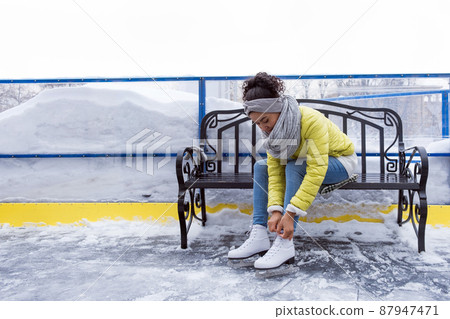 African american woman tying shoelaces on ice skates outdoors African american woman tying shoelaces on ice skates outdoors 87947471