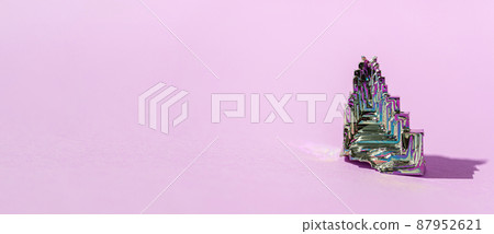 Synthetic bismuth Bismuthum crystal with iridescent oxide film on pink background close up isolated. Amazing colorful shiny rainbow Bismuth Gemstone mineral. 87952621