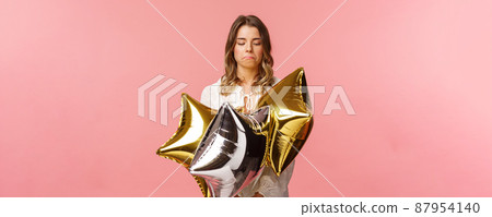Holidays, celebration and women concept. Portrait of satisfied good-looking blond girl make not bad face, pulling lips down and nod in approval, looking at cool star-shaped balloons 87954140