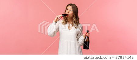 Holidays, spring and party concept. Portrait of young elegant happy blond woman, wear white trendy dress, drinking wine from glass looking up pleased, tasting good drink, hold bottle Holidays, spring and party concept. Portrait of young elegant happy blond woman, wear white trendy dress, drinking wine from glass looking up pleased, tasting good drink, hold bottle 87954142