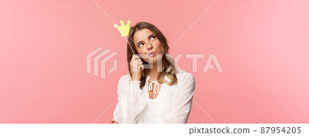 Spring, happiness and celebration concept. Close-up portrait of thoughtful young confident and attractive girl feeling like queen of night party, daydreaming, thinking with crown mask on head Spring, happiness and celebration concept. Close-up portrait of thoughtful young confident and attractive girl feeling like queen of night party, daydreaming, thinking with crown mask on head 87954205