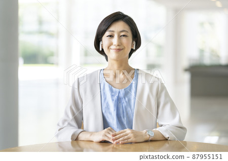 A business woman in her thirties with a smile looking at the camera wearing wireless earphones A business woman in her thirties with a smile looking at the camera wearing wireless earphones 87955151