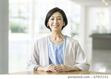 A smiling business woman in her thirties wearing wireless earphones looking at the camera A smiling business woman in her thirties wearing wireless earphones looking at the camera 87955152
