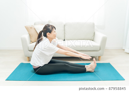 Middle-aged woman doing yoga in the room (forward bending) Middle-aged woman doing yoga in the room (forward bending) 87958845
