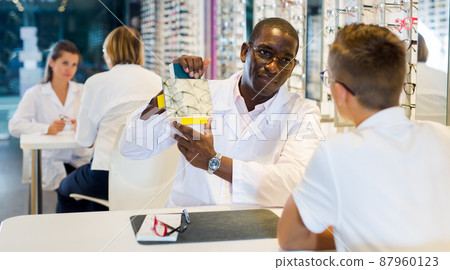 Boy choosing glasses and man ophthalmologist holding mirror Boy choosing glasses and man ophthalmologist holding mirror 87960123