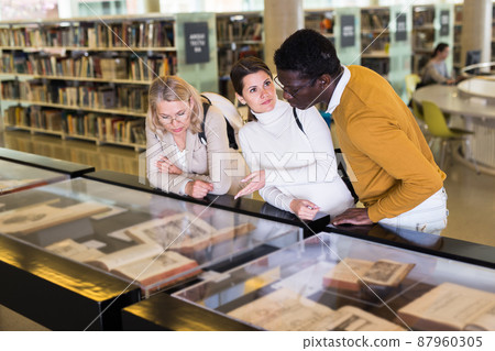 Professor and adult students read ancient books in a library showcase Professor and adult students read ancient books in a library showcase 87960305