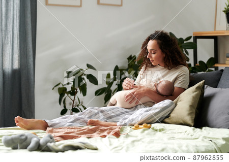 Serene woman with adorable newborn baby son on her hands relaxing on bed Serene woman with adorable newborn baby son on her hands relaxing on bed 87962855