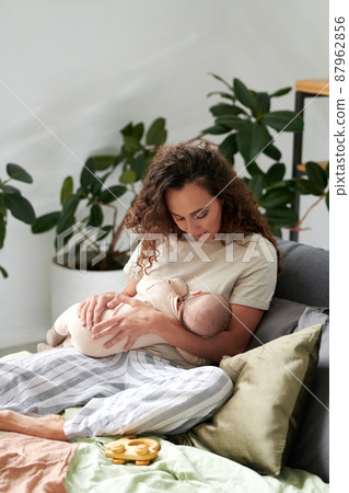 Young mother with newborn baby relaxing by cushions on double bed in bedroom Young mother with newborn baby relaxing by cushions on double bed in bedroom 87962856