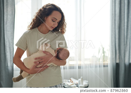 Young serene woman with her baby son by her chest lulling him Young serene woman with her baby son by her chest lulling him 87962860