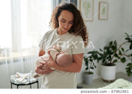 Contemporary young mother holding newborn baby by her chest Contemporary young mother holding newborn baby by her chest 87962861