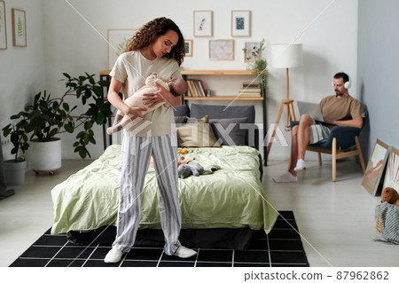 Young female in pajamas lulling baby son against her husband with laptop Young female in pajamas lulling baby son against her husband with laptop 87962862