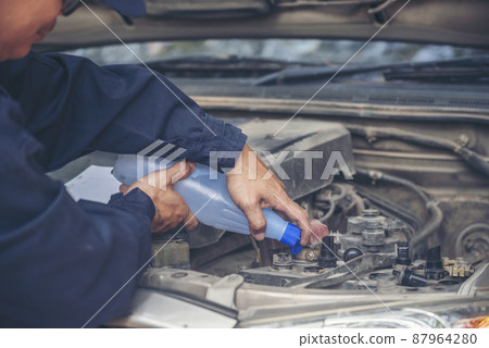 Car Mechanic man hands pouring Deionized purified Distilled water for car battery mechanical service. Close up hands man hold Deionized Distilled liquid water bottle at garage auto mobile car service 87964280