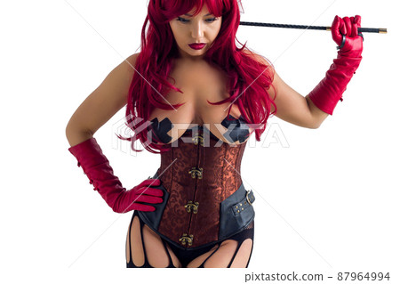 Dominant woman in a red wig corset and leather gloves posing on a white background. 87964994