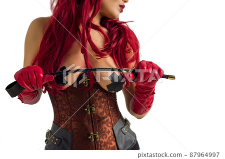 Dominant woman in a red wig corset and leather gloves posing on a white background. 87964997