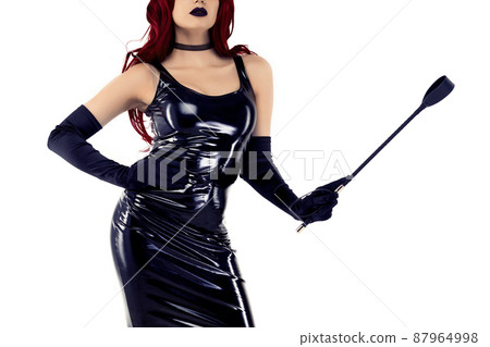 Red-haired passionate lady in a black latex dress posing with a whip in her hands Red-haired passionate lady in a black latex dress posing with a whip in her hands 87964998