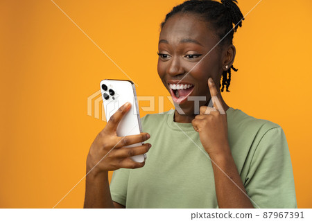 Happy smiling african american girl using her smartphone in yellow studio. 87967391