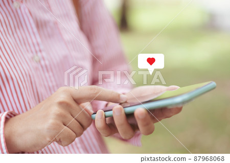 Close up woman hand hold using smart phone with heart icon at outdoor park street background. Copy space of technology business and travel holiday concept. Close up woman hand hold using smart phone with heart icon at outdoor park street background. Copy space of technology business and travel holiday concept. 87968068