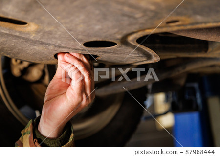 bare caucasian hand unscrews the drain plug of the engine crankcase to change the oil bare caucasian hand unscrews the drain plug of the engine crankcase to change the oil 87968444
