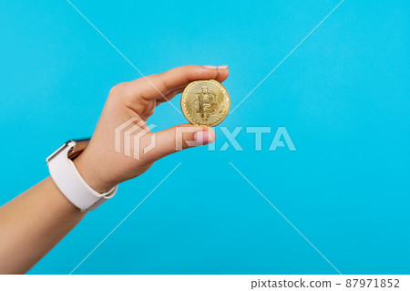 Cryptocurrency. Closeup of female hand with watch holding physical golden bitcoin, advertising of btc crypto coin, digital currency, electronic investment. studio shot isolated on blue background 87971852