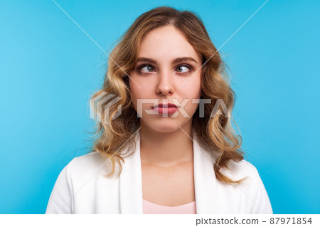 Closeup portrait of adorable funny woman with wavy hair in white jacket looking cross-eyed with awkward silly dumb face expression, squinting eyes. indoor studio shot isolated on blue background Closeup portrait of adorable funny woman with wavy hair in white jacket looking cross-eyed with awkward silly dumb face expression, squinting eyes. indoor studio shot isolated on blue background 87971854