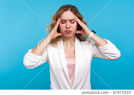 Headache. Portrait of unhealthy girl with wavy hair in white jacket suffering migraine, standing with closed eyes and touching head to relieve pain, feeling sick stressed. studio shot, blue background Headache. Portrait of unhealthy girl with wavy hair in white jacket suffering migraine, standing with closed eyes and touching head to relieve pain, feeling sick stressed. studio shot, blue background 87971910