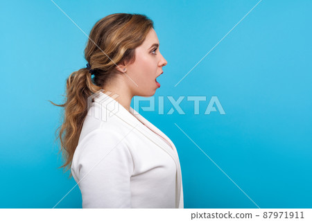 Wow, unbelievable, Side view of amazed woman with ponytail hairdo in white jacket looking with mouth open in surprise, shocked by crazy news. indoor studio shot isolated on blue background, copy space Wow, unbelievable, Side view of amazed woman with ponytail hairdo in white jacket looking with mouth open in surprise, shocked by crazy news. indoor studio shot isolated on blue background, copy space 87971911