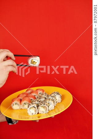 Close up cropped photo of male hold in hands makizushi sushi roll served on plate traditional japanese food isolated on red background in studio. Copy space advertising mock up. 87972001