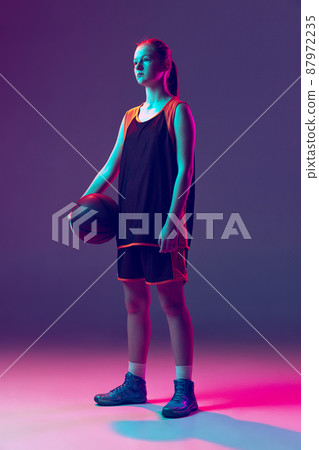 Portrait of young girl, teenager basketball player in uniform posing isolated over gradient pink purple background in neon 87972235