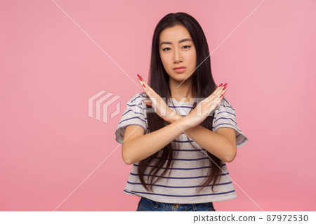 No way, stop doing, Portrait of serious girl with brunette hair in striped t-shirt making x sign with crossed hands, gesturing stop, warning of danger. indoor studio shot isolated on pink background 87972530