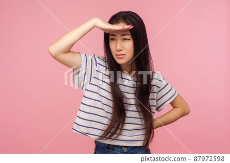 Portrait of young ambitious pretty girl with long hair holding head over eyes and looking into distance with attentive expression, planning future. indoor studio shot isolated on pink background 87972598