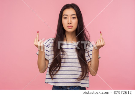 Portrait of annoyed rude vulgar girl with long brunette hair showing fuck off sign, expressing negativity disrespect and hate with middle finger gesture. indoor studio shot isolated on pink background 87972612