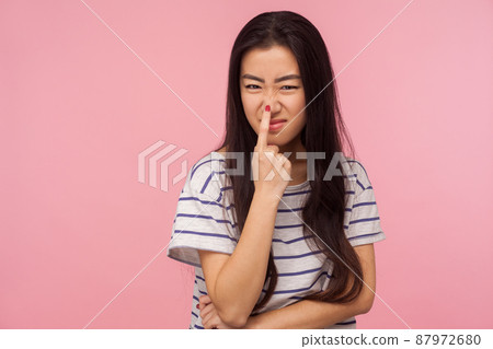 This is lie, Portrait of girl with long hair in striped t-shirt touching nose, gesturing you are liar, being distrustful of talk, suspecting falsehood. indoor studio shot isolated on pink background This is lie, Portrait of girl with long hair in striped t-shirt touching nose, gesturing you are liar, being distrustful of talk, suspecting falsehood. indoor studio shot isolated on pink background 87972680