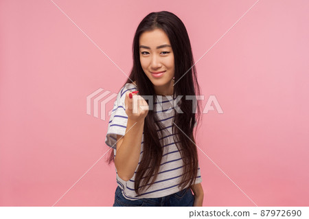 Come here, Portrait of attractive girl with brunette hair in striped t-shirt gesturing come to me, beckoning with finger, inviting for confidential talk. indoor studio shot isolated on pink background 87972690