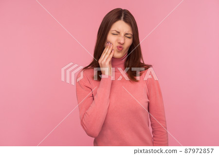 Unhealthy brunette woman touching cheek feeling unpleasant dental pain, oral cavities inflammation, gingivitis. Indoor studio shot isolated on pink background 87972857