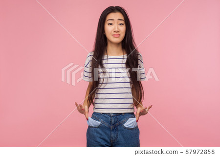 Unemployment and bankruptcy. Upset poor girl with brunette hair in striped t-shirt turning out empty pockets, worried about debts, no cash for living. indoor studio shot isolated on pink background 87972858
