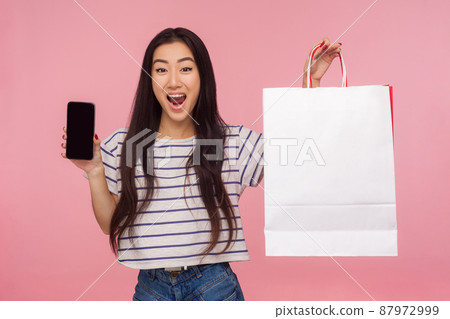 Awesome online purchase, Portrait of excited amazed girl holding cell phone and shopping bags, advertising delivery apps, looking shocked at camera. indoor studio shot isolated on pink background Awesome online purchase, Portrait of excited amazed girl holding cell phone and shopping bags, advertising delivery apps, looking shocked at camera. indoor studio shot isolated on pink background 87972999