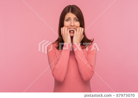 Nervous confused brunette woman in pink sweater biting nails on her fingers in panic, depression, sadness. Indoor studio shot isolated on pink background Nervous confused brunette woman in pink sweater biting nails on her fingers in panic, depression, sadness. Indoor studio shot isolated on pink background 87973070