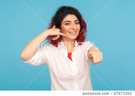 Hey you, call me back. Happy woman with fancy red hair making telephone gesture near head and winking playfully, waiting for call, wants to talk on phone. studio shot isolated on blue background 87973263