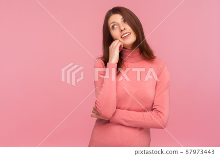 Dreamy optimistic brunette woman in pink sweater leaning head on hand imagining her perfect life, fantasizing. Indoor studio shot isolated on pink background Dreamy optimistic brunette woman in pink sweater leaning head on hand imagining her perfect life, fantasizing. Indoor studio shot isolated on pink background 87973443